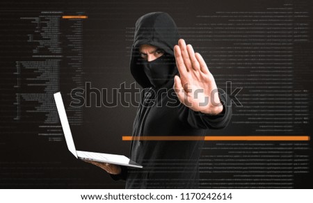 Hacker with his computer making stop sign on dark background