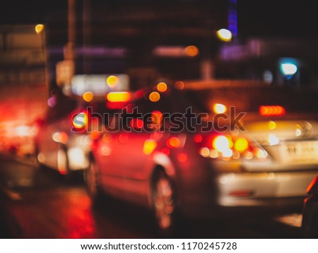 blurred car on the road with red light bokeh and reflection from wet ground after the rain , at night in bangkok thailand