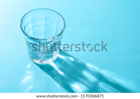 Transparent glass Cup on blue background and long shadow from it with different interesting pictures