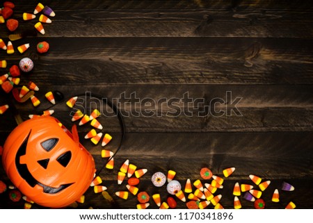 Halloween Jack o Lantern pail with corner border of spilling candy. Above view on a rustic wood background with copy space.