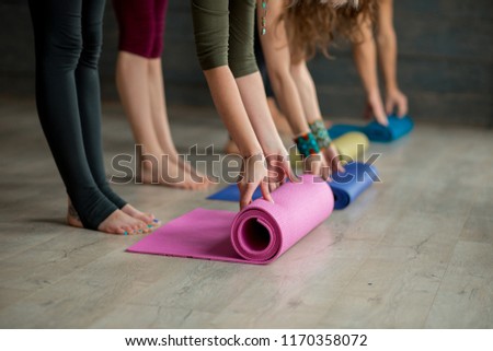 Cropped view of women hands unrolling colourful yoga mats before practicing yoga, preparing for exercise in studio interior