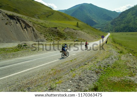 A couple of man and woman in helmets ride on sports bicycles on a road in the mountains of the Altai climbing up