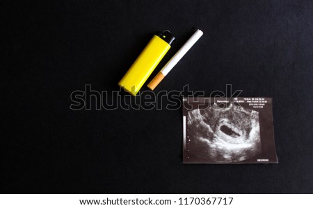 Cigarette and lighter lie on the picture of uzi pregnancy, smoking and pregnancy, gestation, black background