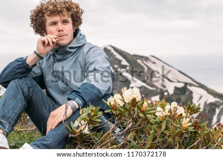pensive tourist is sitting near the wonderful flowers outdoors. close up photo. breathtaking mountaines on the background of the photo. copy space