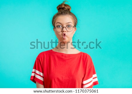 funny girl with hairbun making a funny face, grimace, amazement, joke concepts , isolated blue background,
