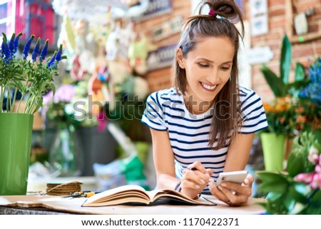 Picture of cheerful florist looking at phone while leaning against counter in her shop
