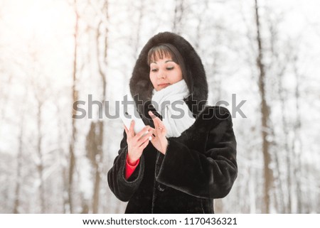 Technology, people and winter concept - Young woman with smartphone and winter landscape snowflakes on the background