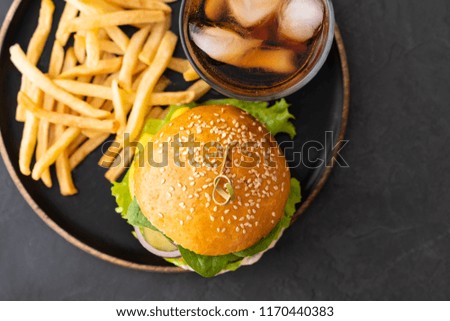 Tasty grilled home made burger with beef, tomato, cheese, cucumber, french fries and lettuce on a dark stone background with copy space. Top view. fast food and junk food concept