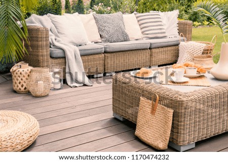 Wicker patio set with beige cushions standing on a wooden board deck. Breakfast on a table on a backyard porch.