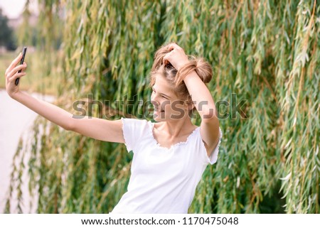 Beautiful young blonde Caucae taking a selfie with smartphone outdoors in park in summer. nature in a park by the river.