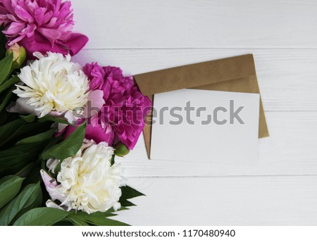 invitation card, craft envelope and pink peony flowers on a white wooden background