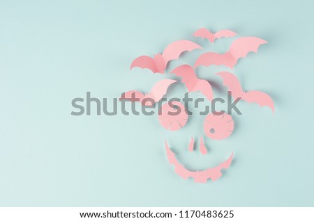 Terrible scary pink face with bats of cut paper on soft light paste blue background. Funny halloween modern concept art backdrop.