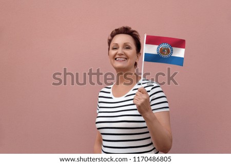 Missouri flag. Woman holding Missouri state flag. Nice portrait of middle aged lady 40 50 years old with a state flag over pink wall on the street outdoors.