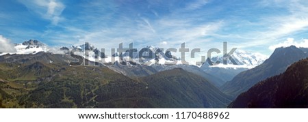 Stunning snow capped peaks of the Alpine ridge of the Mont Blanc Massive. The village of chamonix is visible on the valley floor. The mountain sides are lush green with pine forests on a summer day.