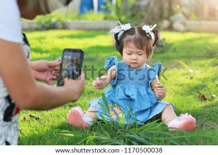 Mother taking a photo with her baby daughter sitting on yard.