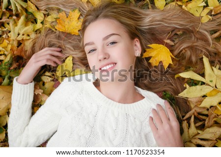 beauty, people, season and health concept - pretty girl is lying in yellow Autumn leaves