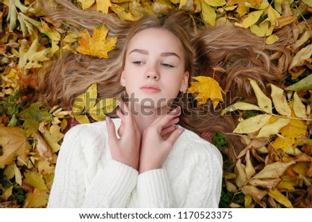 beauty, people, season and health concept - pretty girl is lying in yellow Autumn leaves