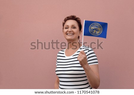 Nebraska flag. Woman holding Nebraska state flag. Nice portrait of middle aged lady 40 50 years old with a state flag over pink wall on the street outdoors.
