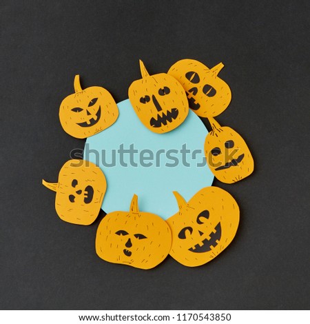 Creative card for invitation for Halloween with handmade paper round frame and yellow smiling scary pumpkins on a black paper, place under text. Flat lay