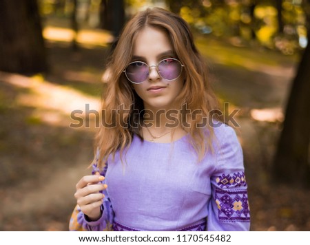 Portrait of cheerful Ukrainian girl wearing national embroidered shirt. Autumn portrait of cute curly teenage girl. Violet sunglasses. 