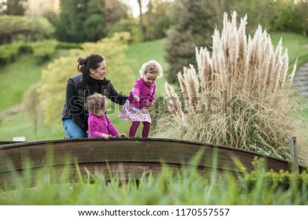 Mother having fun with identical twins on bridge, blond cute girls with mother, happy family, identical twins, beautiful girls in pink jackets and colorful skirts, young family in park in spring