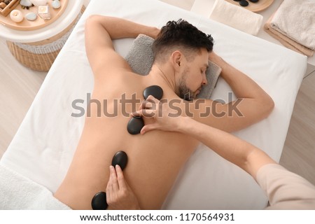 Handsome man having stone massage in spa salon Royalty-Free Stock Photo #1170564931