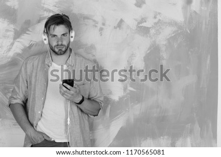 Blue eyed stylish hipster with smartphone. Musical lifestyle. European guy have fun time. Cheerful teenage dj listening songs via earphones. American handsome bearded man with headphones.