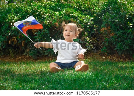 Happy, little kid, cute baby holding Russian flag and seating on green grass outdoor. Patriotic toddler.