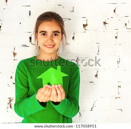 Little smiling brunette girl holding green house in her hands. Concept