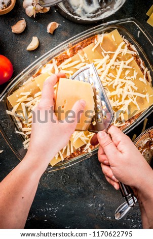 Woman cooking homemade classic lasagna bolognese, on dark blue table; with ingredients, top view copy space, hands in picture