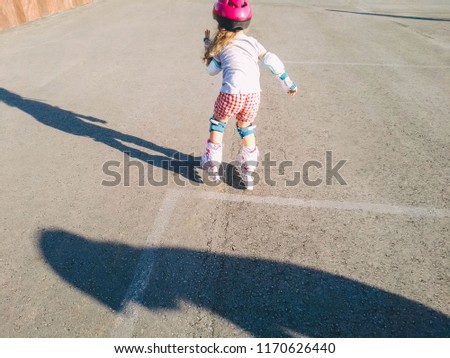 Little girl on roller skates in helmet at a park. Back view.