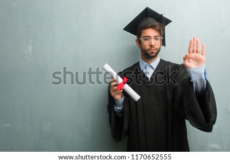 Young graduated man against a grunge wall with a copy space serious and determined, putting hand in front, stop gesture, deny concept