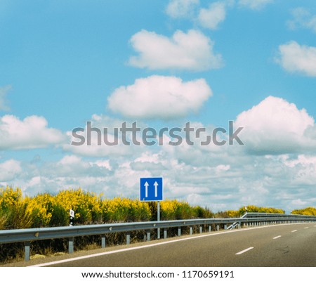 Blue sign pointing up at empty highway with blue sky and fluffly clouds - concepts include: heaven, peace and optimism