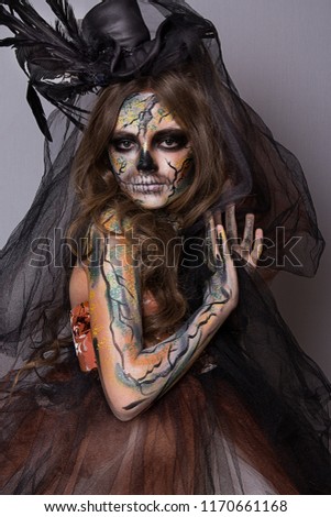 Mystical girl with a painted skull on her face in the style of Halloween in black hat. close up portrait of beautiful girl with professional Halloween makeup
