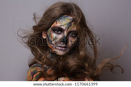 Mystical girl with a painted skull on her face in the style of Halloween. close up portrait of beautiful girl with fluttering hair. professional Halloween makeup