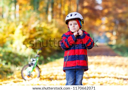 Active child putting safe helmet before cycling on sunny fall day in nature.