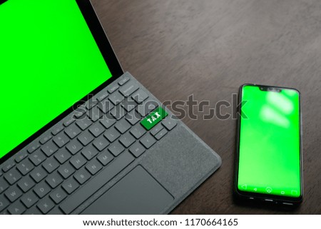 TAX Key on tablet cover keyboard with green screen on tablet screen and smartphone. A business and finance conceptual