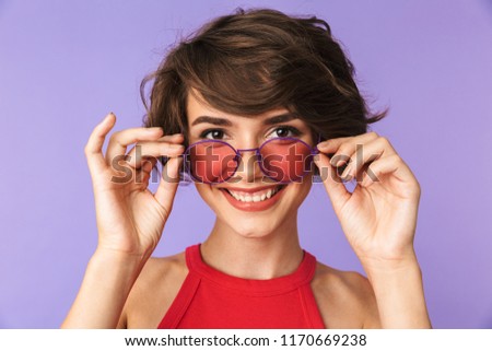 Image of cheerful woman 20s in casual wear and sunglasses looking at you with smile isolated over violet background