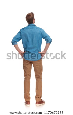 back view of a casual man with hands on waist standing and looking up on white background Royalty-Free Stock Photo #1170672955