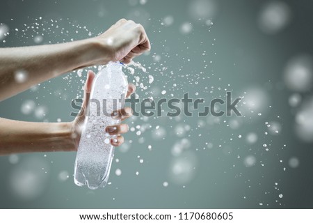 Woman's hand opening a bottle with sparkling water with splashes and lot of drops on gray background. Studio photo shooting. Concept of health lifestyle Royalty-Free Stock Photo #1170680605