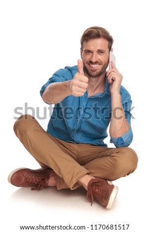 young happy seated casual man talks on the phone and makes the ok sign on white background