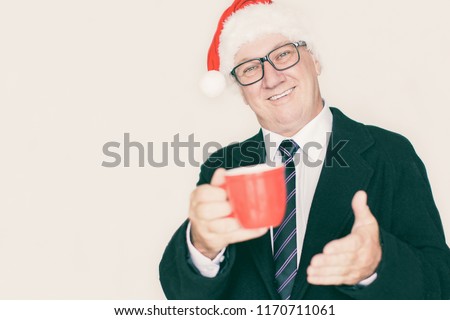 Cheerful pleased businessman in Santa hat offering cup of coffee and looking at camera. Happy handsome male employee drinking coffee. Job at holidays concept