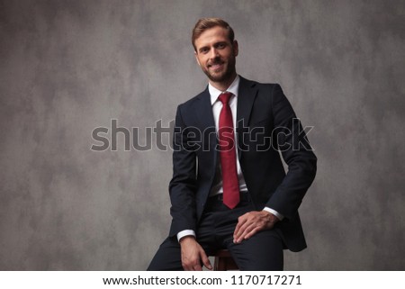 smiling young businessman sitting on a stool , studio picture
