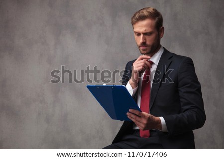 confused young businessman is reading data on a clipboard and thinks , studio picture