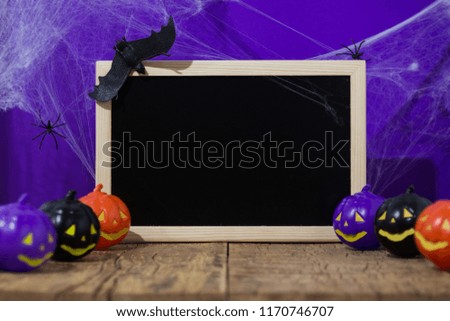 Halloween background decor holiday concept. Blackboard with decor pumpkin, bat, snake spider, cobweb on wooden table and purple backdrop