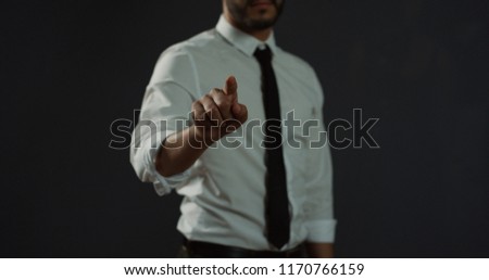 Posture of the man in the white shirt and tie scrolling and typing with his finger in the air like having a hologram screen in front of him on the black background.