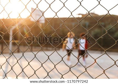 Group of young cheerful multiethnic men basketball players playing basketball at the sport ground, focus on fence