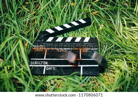 Black clapperboard with film lying on the grass in the nature outdoors. Directing and of amateur cinema movie. Creative concept. Retro vintage photo.