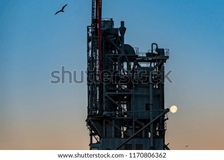 Detail of dock loading equipment with seagulls in flight and moon in the background, right before sunrise.