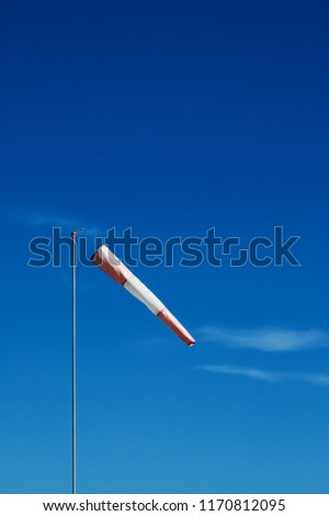 Red and white windsock on a pole with blue sky in background